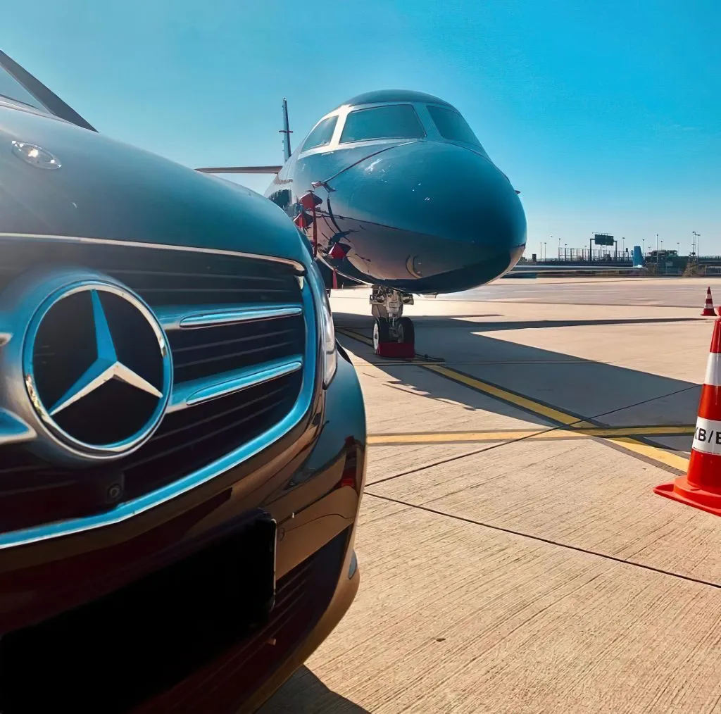 NCC-licensed luxury Mercedes waiting on the tarmac at Olbia Costa Smeralda Airport for an exclusive private transfer in Sardinia, positioned next to a business jet.
