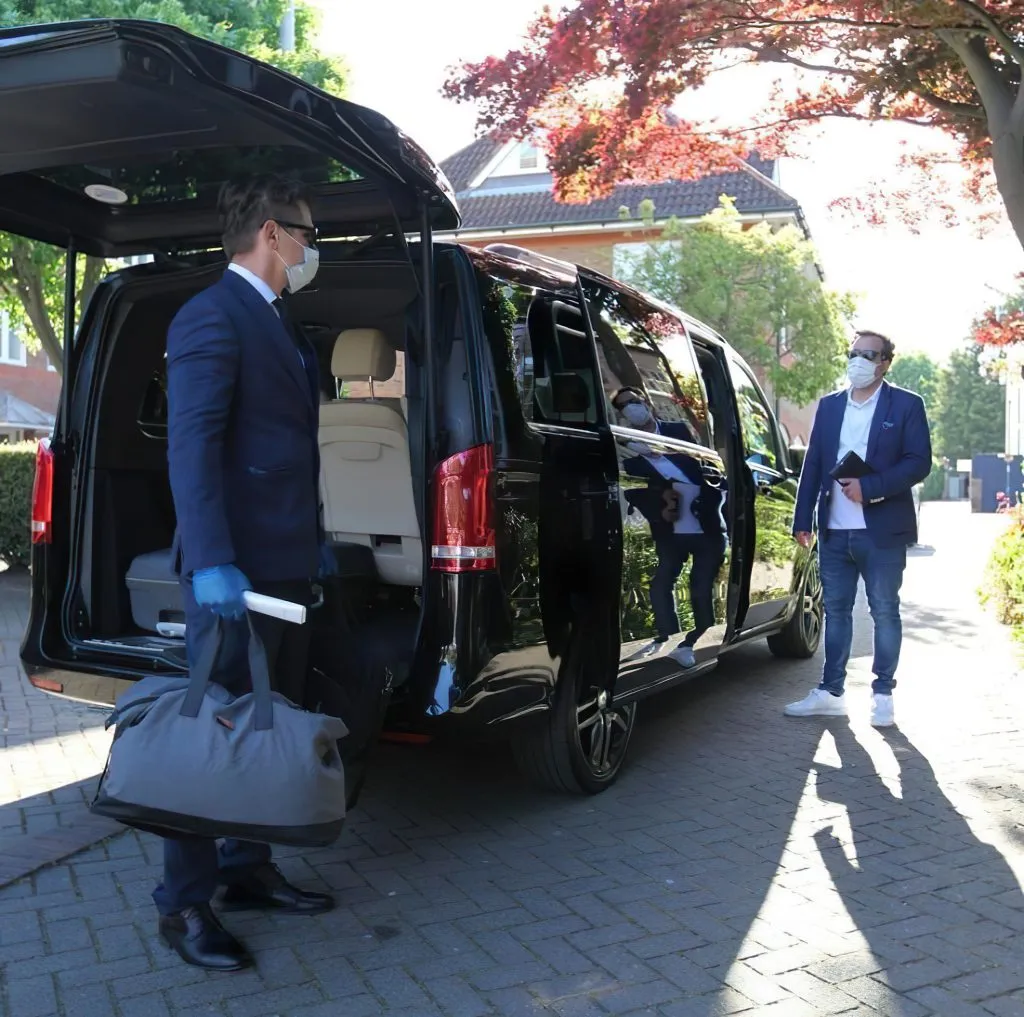A professional driver in Sardinia providing premium luggage assistance to a traveler by a luxury black Mercedes minivan, showcasing the reliable service of Sardinia Airport Transfer.