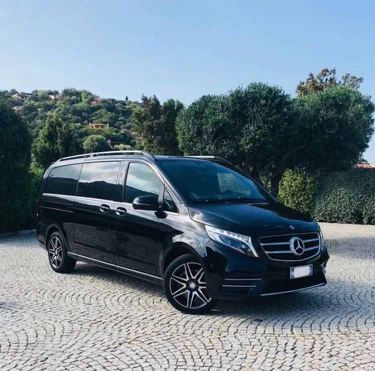 A premium black Mercedes-Benz V-Class parked on a cobblestone driveway in a lush Sardinian landscape, representing the high-standard fleet for private airport transfers.